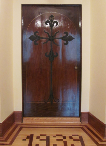 Rectangular wooded door.Fixed on it, a large iron cross. On the floor, a wooden floor covering on With light and dark slate forming the year: 1639