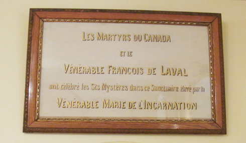 Frame. In golden letters « Les Martyrs du Canada et le Vénérable Francois de Laval ont célébré les Sts Mystères dans ce Sanctuaire élévé par la Vénérable Marie de l’Incarnation ».