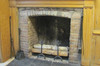 Red brick hearth, encased in a wooden wall. Cemter: wood logs. At the left against the wall, tools for the fire and fireplace maintenance.