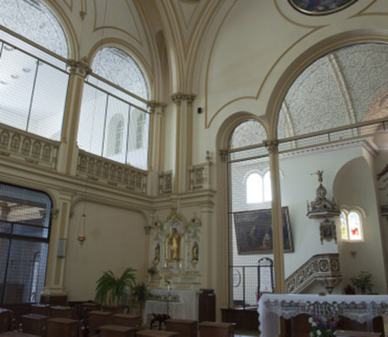 Coin de la chapelle. Vue des grilles. Ouverture centrale vers un autel. Grilles supérieures décoratives à volutes, en arc.
