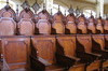 Two rows of wooded ornamented chairs. More than forty chairs. Last row chairs have taller arched back with decorative spindle up their back.