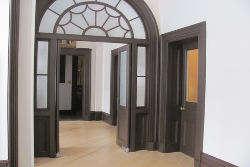 Portes brunes ouvertes. En haut, fenêtres de verre, décoratives, en arc. Sur la droite, porte brune fermée.