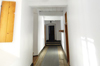 Corridor blanc terminant par 3 marches et une porte. Plancher de larges planches de bois. Plafond de bois peint blanc, poutres apparentes. 