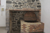 Room with vaulted white ceiling. Gray floor. Wall of gray stones. Brick vat looking like a big pot.