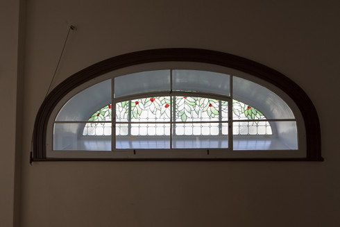 Vitrail en demi-ovale. Premier plan : fenêtre à carreaux. Fond : Vitrail artistique de feuilles et de fruits rouges sur motif de grille.