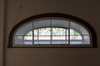 Semi-oval stained glass. Foreground: checked window. Background: Artistic stained glass of leaves and red fruits on grid pattern.