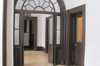 Portion of white corridor. Arch of brown wood and glass. Separates 2 brown doors, glazed. In the background, the corridor of the chLonapels.