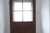 Porte brune, simple. Fenêtre au centre. 4 carreaux. Entourée de murs blancs. 