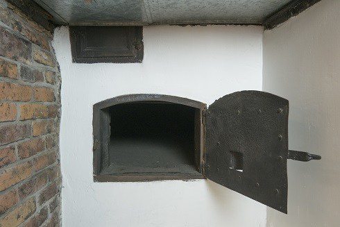 White wall with a bread oven opening. A Small iron-cast door is open. The left wall is made of red bricks.
