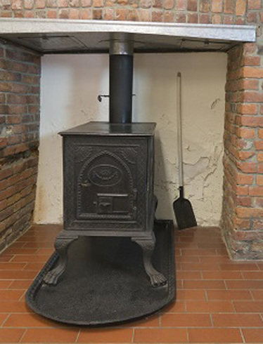 Long white corridor. Wooden door on the left. Large slate floor covered by a long grey carpet. At the middle, the ceiling become vaulted and the floor in stone.