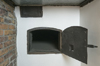 Small open metal door on a white wall and brick. The rectangular opening at the rounded top is that of the old bread oven.