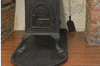 Alcove of bricks housing a stove in cast iron. To the right, an ash shovel hangs on the white wall.