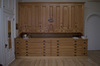 Grand meuble de bois faisant la surface du mur. Tiroirs plats en bas et de grandeurs variées en haut. Au centre, crucifix et tabernacle. 