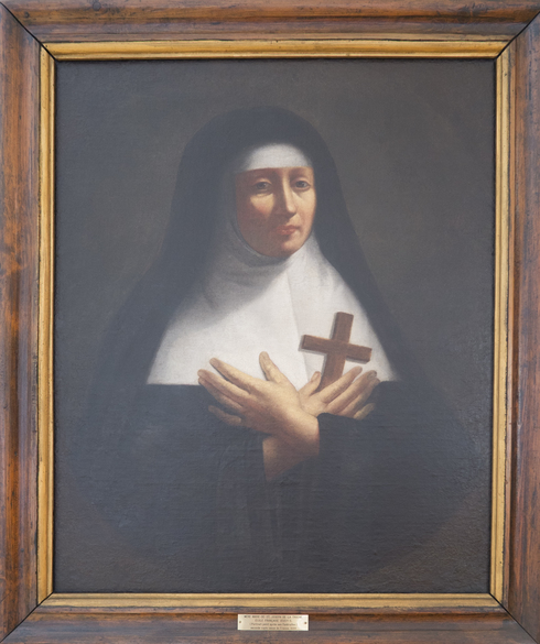 Tableau peint. Portrait de mère St-Joseph. Religieuse : robe et voile noir. Guimpe et bandeau blanc. Mains croisées sur son cœur. Tient une croix de bois.