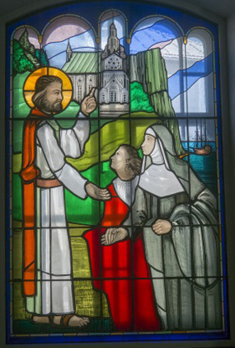 Vitrail rectangulaire, haut en arc. Très coloré. Illustration de Jésus montrant le monastère à Marie de l’Incarnation.